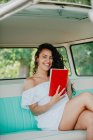 Alegre jovem mulher sentada dentro retro caravana e segurando livro — Fotografia de Stock