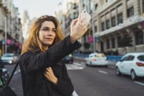 Mulher tirando selfie com smartphone na estrada na cidade — Fotografia de Stock