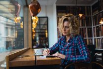 Mujer sentada en la cafetería y escribiendo en cuaderno - foto de stock