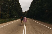 Homem com bandeira dos EUA correndo ao longo da estrada — Fotografia de Stock
