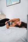 Молода жінка лежить в ліжку і використовує мобільний телефон — стокове фото