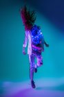 Jeune femme méconnaissable secouant les cheveux et sautant dans la lumière ultraviolette et néon — Photo de stock