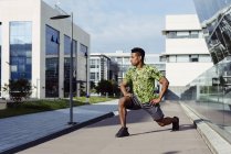 African American man warming up legs in city with modern buildings on background — Stock Photo