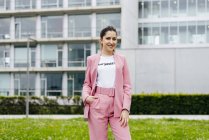 Stylish young woman in pink standing in front of modern office building — Stock Photo