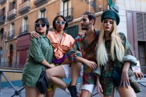 Gruppe junger Leute in trendigen Outfits sitzt auf einem Zaun an der Stadtstraße und schaut weg — Stockfoto