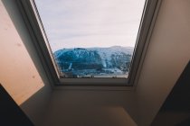 Landscape of snowy mountains through glass window in mansard roof in sunlight — Stock Photo