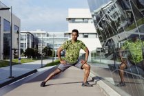 Afro-Américain échauffer les jambes dans la ville avec des bâtiments modernes sur fond — Photo de stock