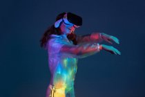 Woman touching air in VR glasses in neon light on dark blue background — Stock Photo