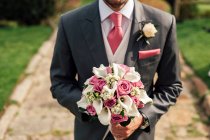 Обрізати красивого чоловіка в сірому костюмі, що стоїть з купою рожевих і білих квітів . — стокове фото