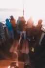 Crop travelers legs and group of tourists on beak of sailing boat in bright sunlight floating on water — Foto stock
