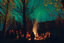 Grupo de personas realizando auténticos rituales alrededor de fuego ardiente y chispeante en bosques oscuros con cielo estrellado - foto de stock
