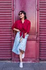 Schöne junge Frau in trendigem Outfit lacht und schaut weg, während sie sich an die Burgundermauer in der City Street lehnt — Stockfoto