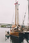 Vista del gran barco de madera en el puerto con marinero sentado cerca en día nublado - foto de stock