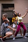 Группа молодых людей в модных нарядах смеется и делает селфи, веселясь на городской улице — стоковое фото