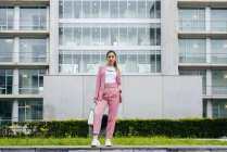 Stylish woman in pink suit standing in front of modern office building — Stock Photo