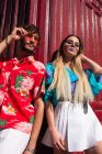 Dal basso colpo di giovane uomo e donna in abiti alla moda appoggiati a muro di colore bordeaux mentre in piedi sulla strada nella giornata di sole — Foto stock