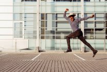 Молодий афро-американський чоловік у капелюсі стрибає високо під час прогулянки по вулиці — стокове фото