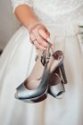 Crop unrecognizable bride holding and showing gray silver shoes. — Stock Photo