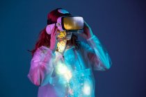 Woman using VR glasses in neon light on blue background — Stock Photo