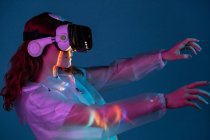 Женщина касается воздуха в VR очках в неоновом свете — стоковое фото