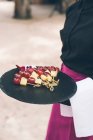 Неузнаваемый официант держит поднос с виноградной лозой и сырной канапе. — стоковое фото