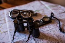 Planning a trip on a map with vintage motorcycle glasses, old photo camera, prismatic and compass — Stock Photo