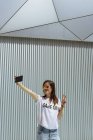 Веселая женщина делает селфи и позирует возле современной стены — стоковое фото