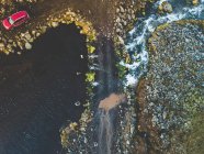 Drone vista della costa rocciosa e torrente d'acqua che scorre tra le pietre con auto rossa parcheggiata sulla riva — Foto stock