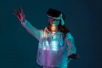 Mujer tocando el aire con gafas VR en luz de neón sobre fondo azul - foto de stock