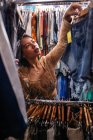 Attraktive junge Dame sucht neues Outfit auf Kleiderstange in kleinem Laden — Stockfoto