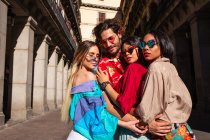 Красивий молодий чоловік обіймається з трьома жінками в модному одязі і стоїть на вулиці в сонячний день — стокове фото