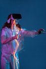 Mulher tocando ar enquanto tem experiência de realidade virtual em luz de néon — Fotografia de Stock