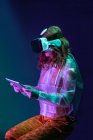 Молода жінка в віртуальної реальності окуляри Холдинг планшет, сидячи в неонові світло — стокове фото