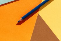 Lápiz azul, sobre fondo geométrico amarillo claro y naranja, vuelta al concepto escolar - foto de stock