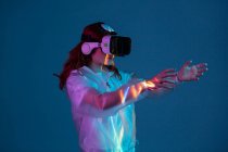 Woman touching air while having virtual reality experience in neon light — Stock Photo