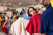 Красивый мужчина выбирает стильную рубашку, проводя время в маленьком магазине с подругой — стоковое фото