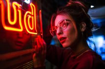 Seitenansicht der attraktiven Frau in Brille mit geschlossenen Augen lehnt an der Wand bei Beleuchtung Leuchtreklame — Stockfoto