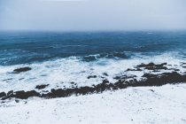 Paisaje de olas frías del océano corriendo contra la costa rocosa nevada en la niebla - foto de stock