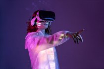 Femme en lunettes VR pointant tout en se tenant dans la lumière au néon — Photo de stock