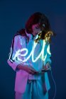 Woman listening to music and using smartphone in neon light inscription — Stock Photo