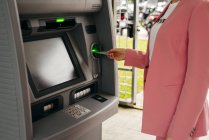Nahaufnahme einer Frau im rosafarbenen Anzug, die auf der Straße eine Kreditkarte in einen Geldautomaten steckt — Stockfoto