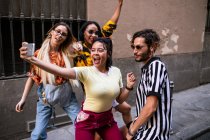 Група молодих людей в модних вбраннях сміється і приймає селфі, розважаючись на міській вулиці — стокове фото