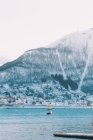 Vista do barco à vela em água azul no fundo da pequena cidade na costa com montanha nevada acima — Fotografia de Stock