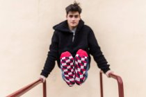 Молодий підліток розробляє і показує барвисті візерункові шкарпетки на бежевій стіні — стокове фото