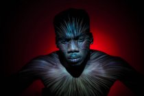 Етнічний чоловік без емоцій стоїть зі світловими лініями на тілі і дивиться на камеру — стокове фото
