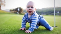 Young boy sitting on green lawn at the hole in golf club and looking at camera. — Stock Photo