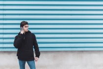 Молодой подросток, стоящий у металлической стены и разговаривающий по мобильному телефону — стоковое фото