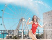 Stylish young woman in red swimsuit standing on terrace with cityscape on background — Stock Photo