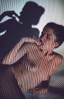 Jovem mulher sedutora nua posando em estúdio com sombra listrada no rosto e corpo — Fotografia de Stock
