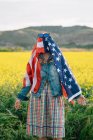 Senhora em roupas casuais ficar em campo amarelo com óculos de sol sobre bandeira americana com luz solar — Fotografia de Stock